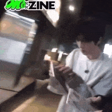 a man in a white shirt is standing in a dark room looking at a cell phone .