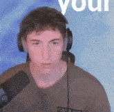 a young man wearing headphones and a microphone is standing in front of a blue background .