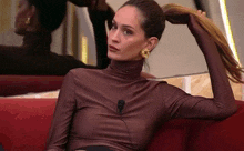 a woman in a brown turtleneck is sitting on a red couch .