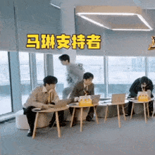 a group of people are sitting at tables with laptops in an office with chinese writing on the ceiling