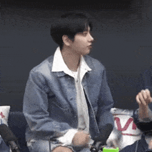 a young man in a denim jacket is sitting in front of a microphone in a room .