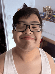 a young man wearing glasses and a white tank top smiles