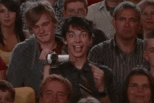 a man in a crowd is holding a camera up to his face