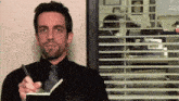 a man in a black shirt and tie is taking notes in a notebook .