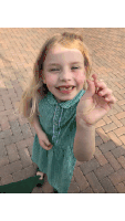 a little girl in a green dress is holding up a tooth