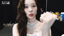 a woman in a white dress and necklace is making a heart shape with her fist .