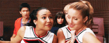 two cheerleaders are standing next to each other in a room with a group of people .