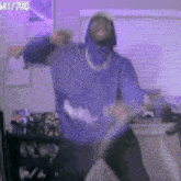 a man in a blue hoodie is dancing in a room with purple walls