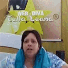 a woman wearing a blue scarf is sitting on a bed in front of a sign that says web diva