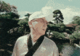 a man wearing a white hat and sunglasses is standing in front of a pond