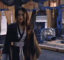 a woman with long hair wearing a kimono is standing in a room