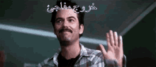 a man with a mustache is waving his hand in a room with arabic writing on it .