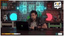 a man is sitting in front of a laptop with a wanted sign on the wall behind him