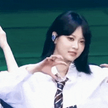 a girl in a white shirt and tie is making a heart with her hands .