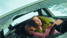 a woman with green hair is sitting in a car with a broken windshield