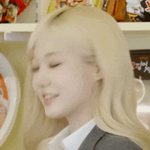 a woman with blonde hair is smiling in front of a shelf full of food