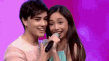 a boy and a girl are standing next to each other and singing into a microphone .