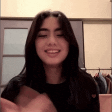 a young woman with long black hair is smiling and making a heart shape with her hands in front of a closet .