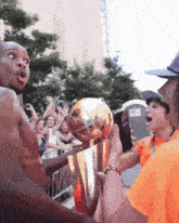 a man in an orange shirt is holding a trophy in front of a crowd of people
