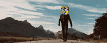 a man is walking down a dirt road with a cartoon cat on his head