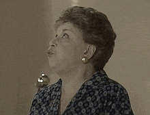 an older woman wearing a black shirt with circles on it looks at the camera