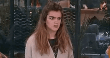 a young woman with long hair is sitting in front of a glass door making a funny face .