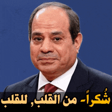 a man in a suit and tie stands in front of a blue background with arabic writing on it