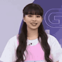 a woman with long hair is wearing a pink apron and a white shirt and smiling .