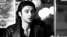 a man in a leather jacket is looking at the camera in a black and white photo .