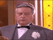 a man in a suit and bow tie has a white flower in his pocket