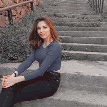 a woman sits on a set of stairs wearing a blue shirt and black jeans