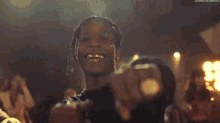 a man with a ring on his finger is pointing at the camera in a crowded room .
