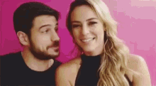 a man and a woman are standing next to each other in front of a pink wall .