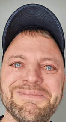 a man with a beard and blue eyes is wearing a hat and making a funny face