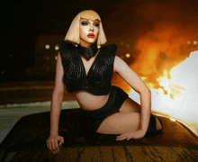 a woman in a black top and shorts sits on a car hood