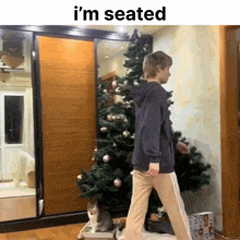 a person standing in front of a christmas tree with the words i 'm seated on the bottom