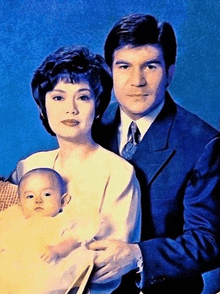 a man and woman holding a baby in front of a blue backdrop