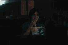 a woman is eating popcorn while watching a movie in a dark theater