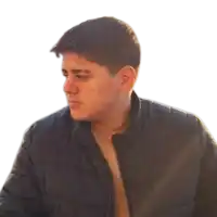 a shirtless man wearing a black jacket looks to the side