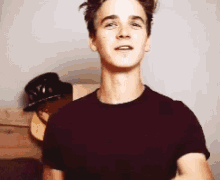 a young man wearing a maroon t-shirt is standing in front of a hat hanging on a wall .