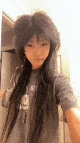 a woman with long hair is taking a selfie in front of a mirror while wearing a gray t-shirt .