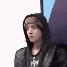 a young man wearing a hooded jacket and a beanie is standing in front of a wall .