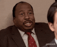 a man in a suit and tie is making a funny face while talking to another man .