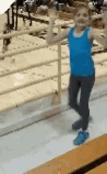 a young girl in a blue tank top and leggings is standing on a trampoline .