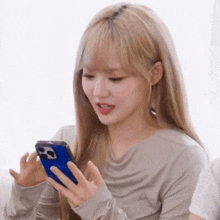 a woman with blonde hair is holding a cell phone in her hand .