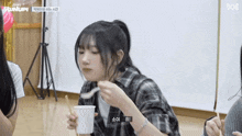 a girl in a plaid shirt is eating from a cup with a spoon