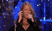 mariah carey is singing into a microphone on a stage .