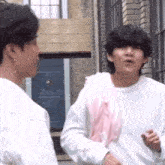 two men are standing next to each other in front of a building and talking .