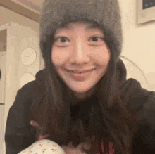 a woman wearing a hat and a black hoodie is smiling and holding a baby .
