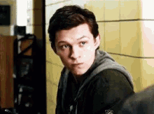 a young man in a hoodie is standing in front of a yellow wall .